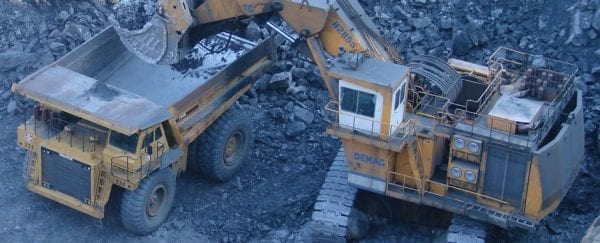 An excavator dumps raw ore into a large dumptruck